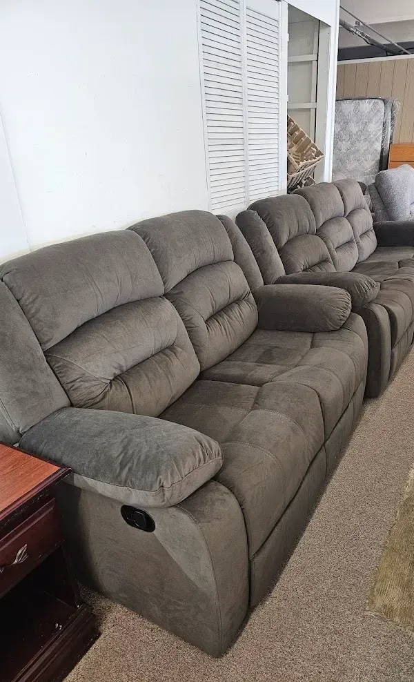 Gray reclining sofa in a furniture showroom with carpeted floor and a mirrored wall behind it