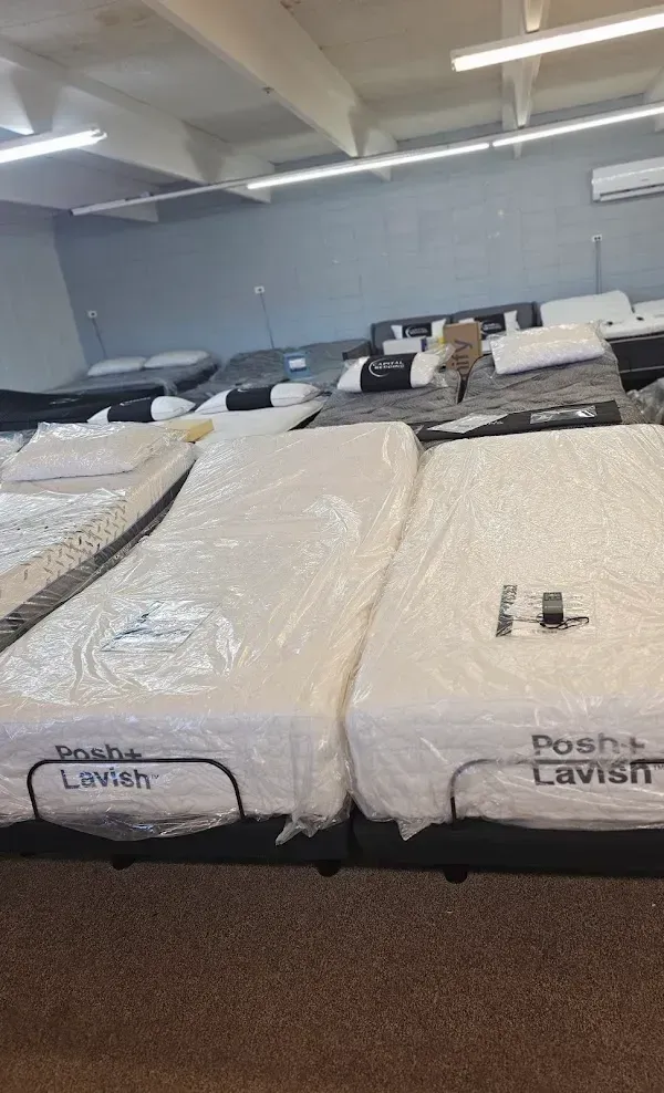 Mattresses in a showroom, wrapped in plastic, with labels visible on the front edges.