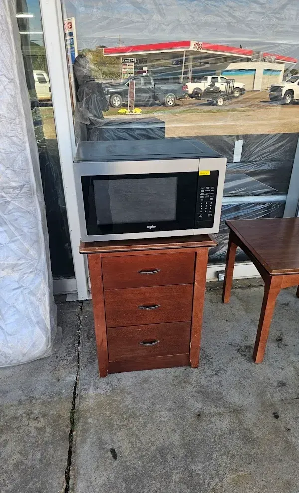 Microwave on a small wooden cabinet beside a chair, in front of a window with a street view