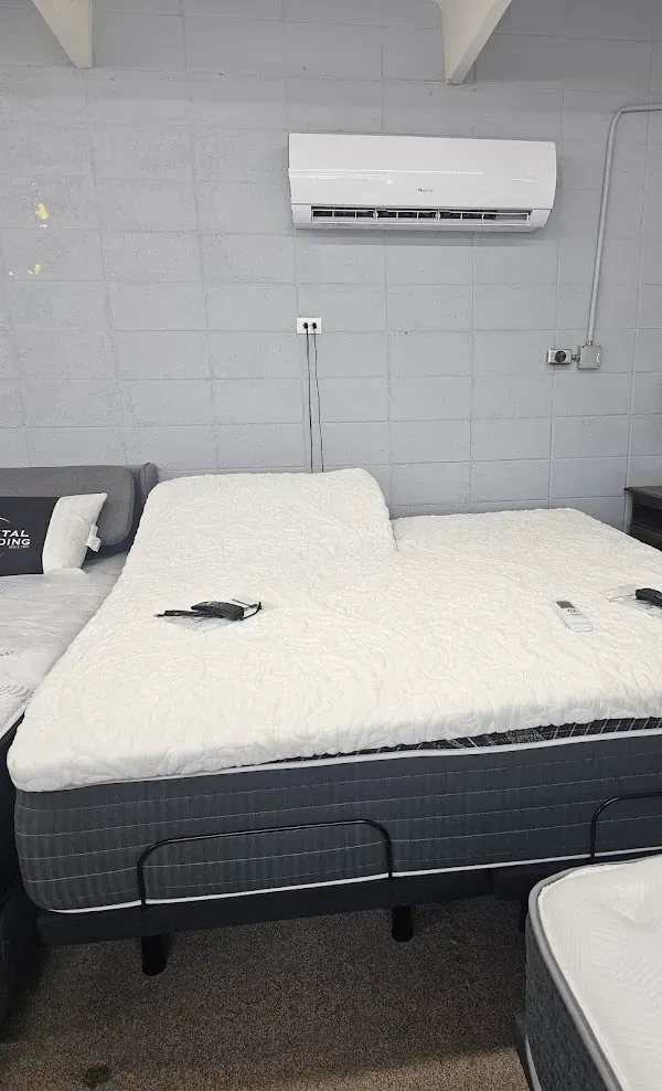 Hospital room with two beds, white bedding, gray tiled walls, and a wall-mounted air conditioner.
