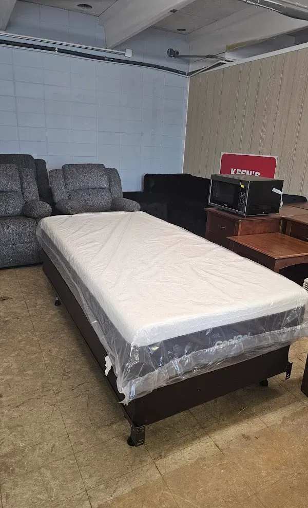 Basement room with a bed, gray couch, desk, and boxes against unfinished walls