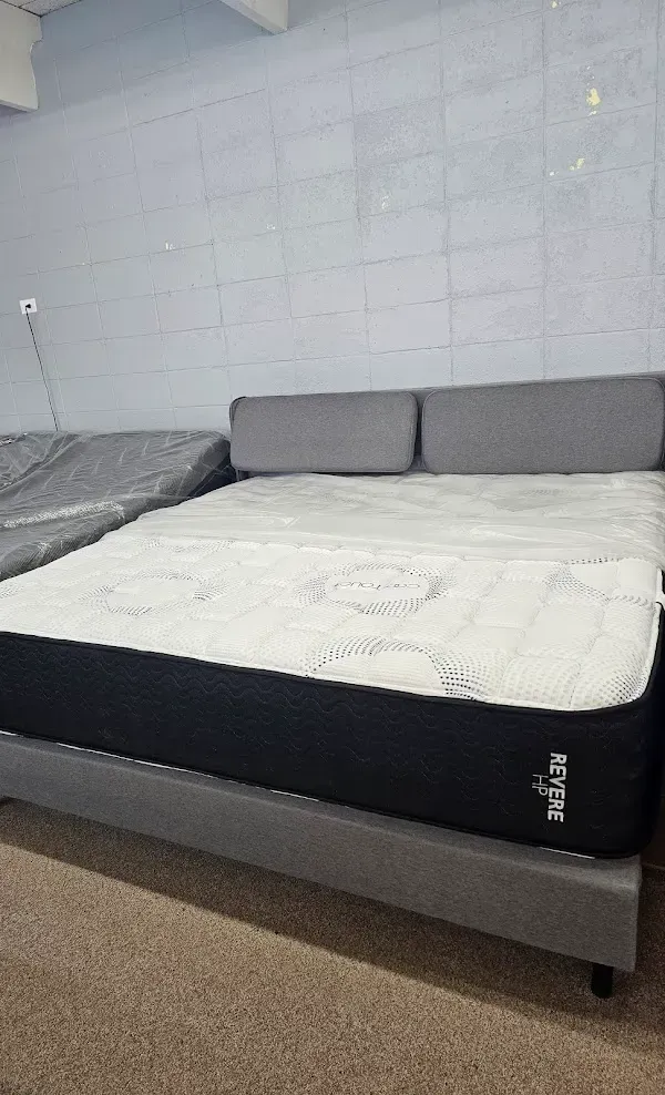 A simple bedroom with a low bed, white mattress, gray pillows, and a cinderblock wall.