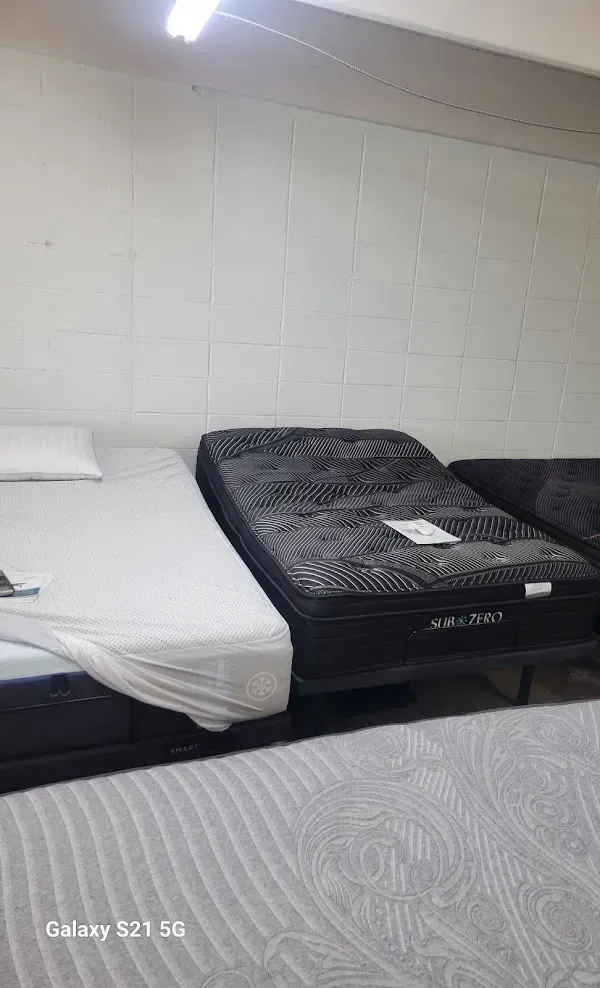 Two beds in a plain room, one made with white sheets and one with a black mattress topper