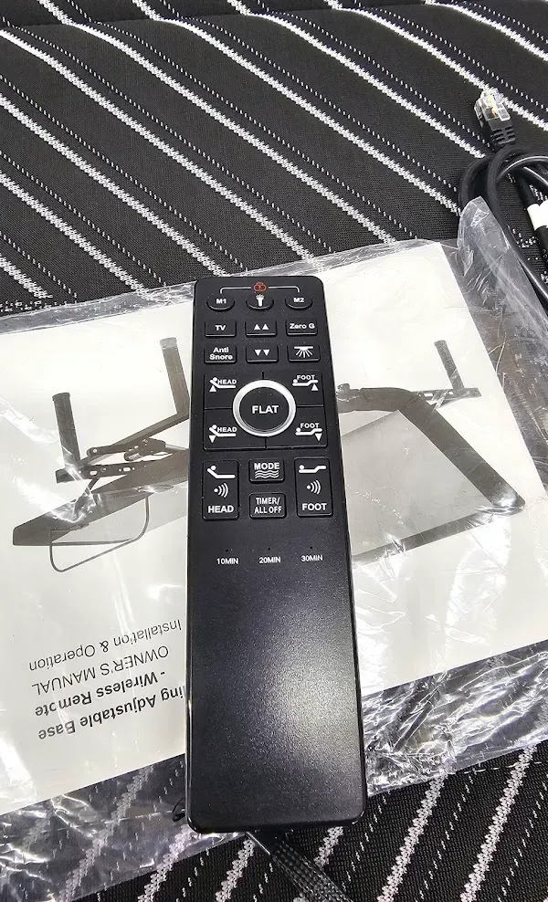 Black TV remote on packaging with two black stands on a striped surface.