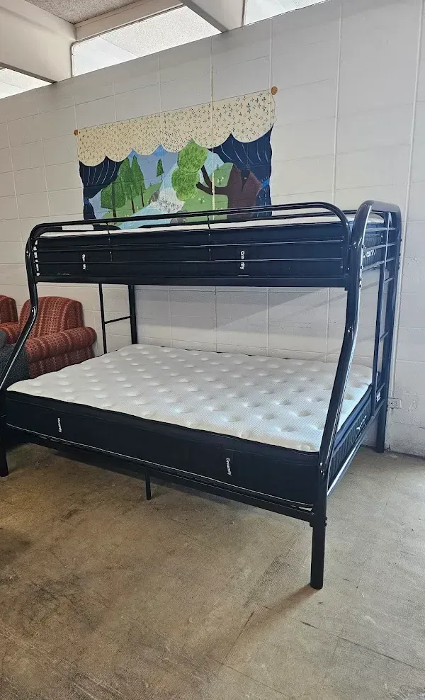 Black metal bunk bed with white mattresses in a tiled room, with a small shelf and wall hanging above.