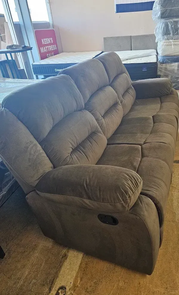 Gray fabric loveseat in a furniture showroom, angled view with cushioned back and armrests.