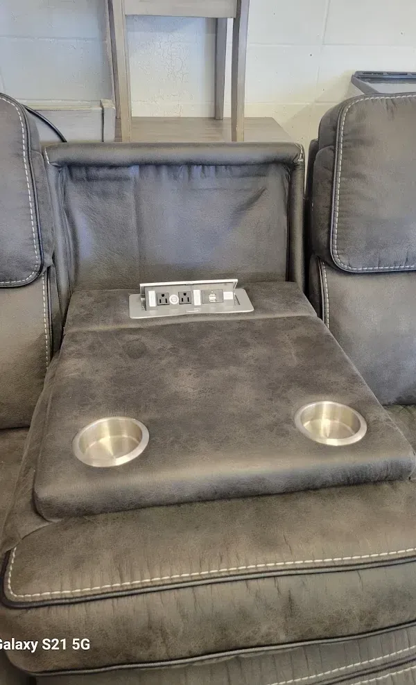 Gray leather theater loveseat with two cup holders and a center control panel against a wall.