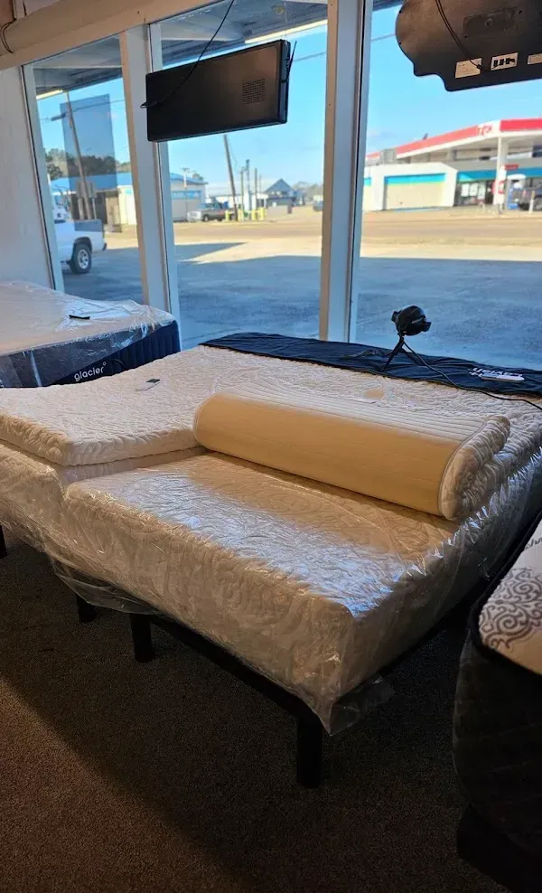 Bed covered in clear plastic inside a storefront with large windows facing a parking lot.