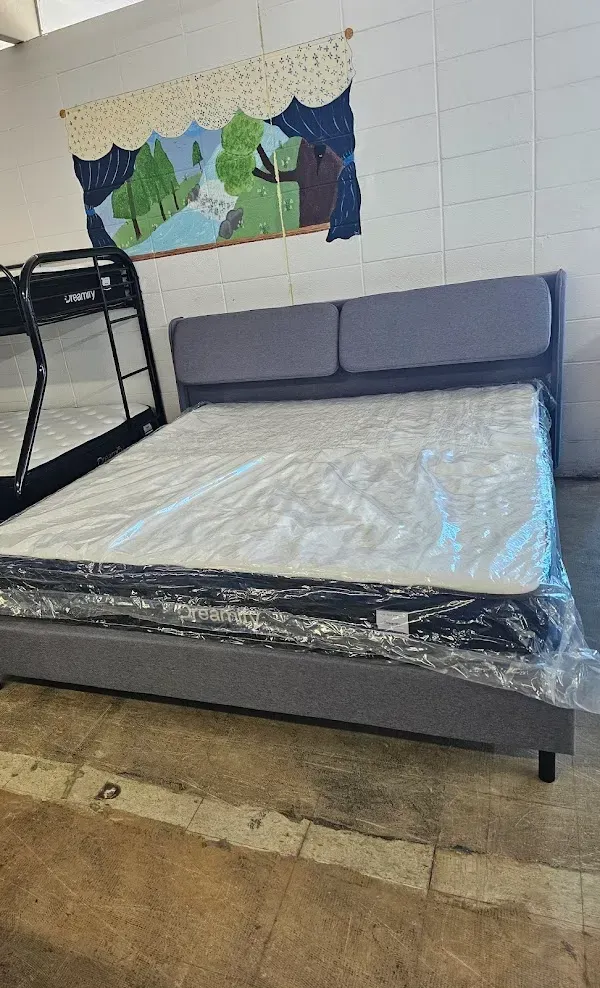 Gray bed with plastic-covered mattress and a colorful wall mural in a sparse room