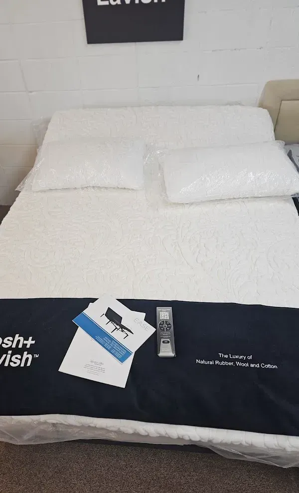 White bed with two pillows and a dark runner holding brochures and a remote control in a showroom.