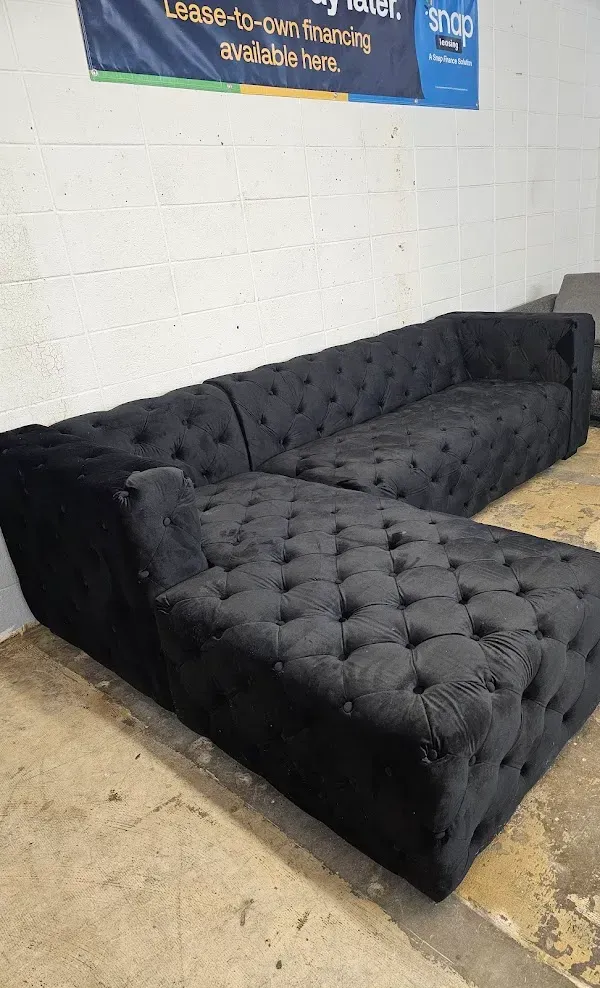 Black tufted sectional sofa in a room with white walls and a tiled floor