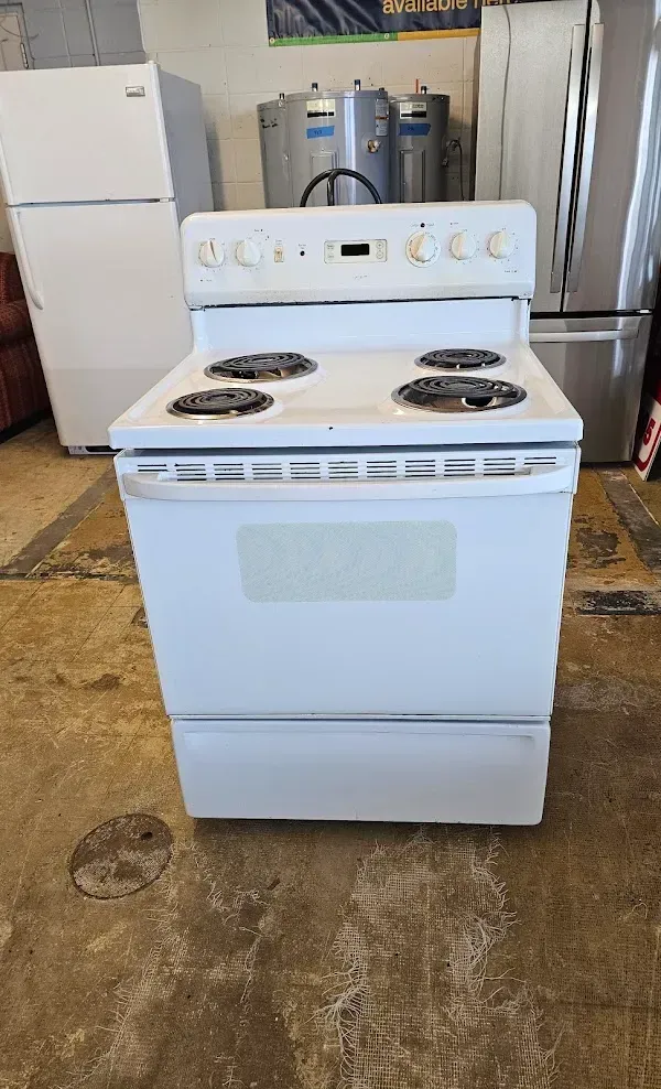 White electric stove in a warehouse, with four burners and oven door visible.