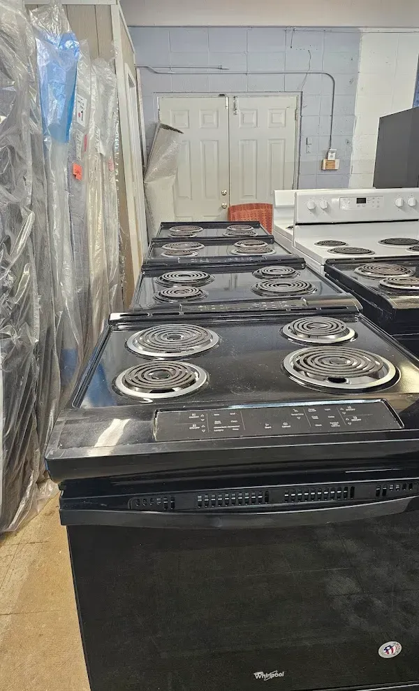 Row of black gas stoves wrapped in plastic, lined up in a warehouse-like room.