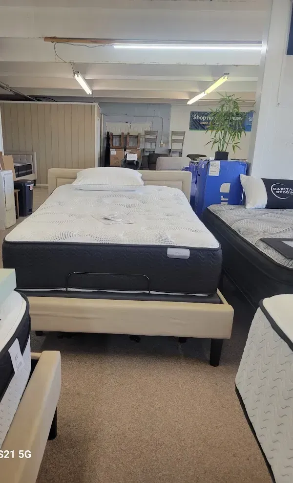 Mattress display in a showroom with several beds arranged in rows under bright ceiling lights.