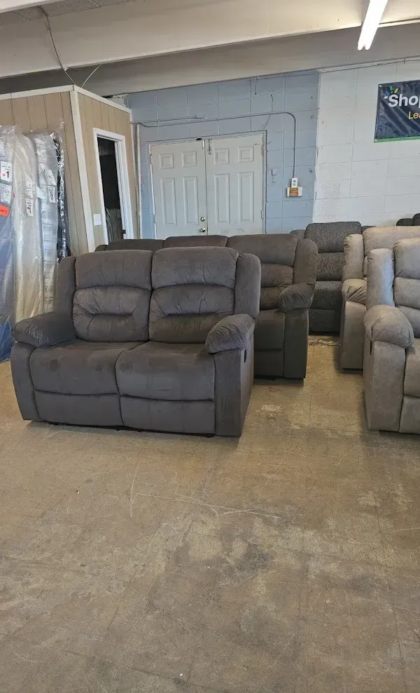 Two gray recliner sofas in a warehouse showroom with concrete floor and shelving in the background
