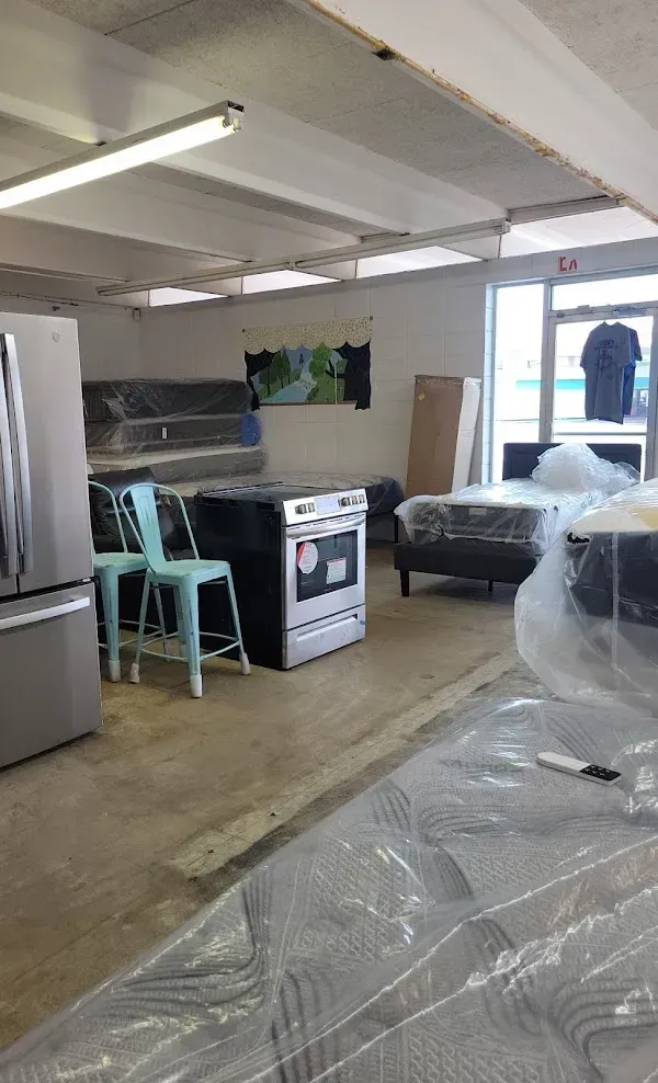 Basement room with refrigerator, stove, chairs, couch, and plastic-covered furniture under fluorescent lights