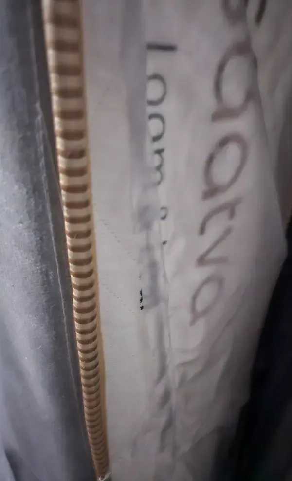 Close-up of white fabric with partial handwritten text beside a beige zipper.