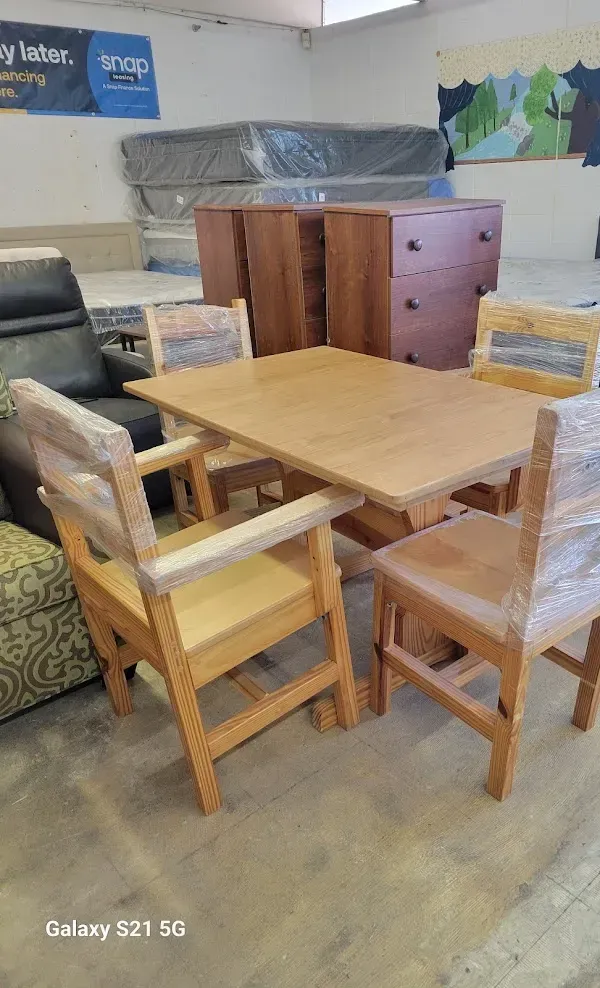 Wooden dining table and chairs in a cluttered room, with a dresser and covered furniture in the background.