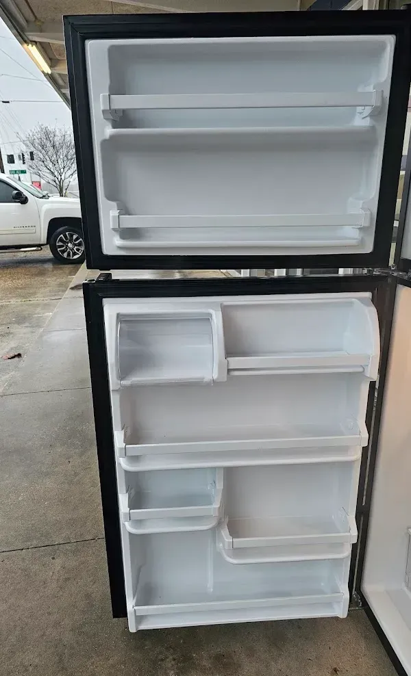 Open mini fridge with white interior shelves and door bins, standing outdoors on a concrete surface.