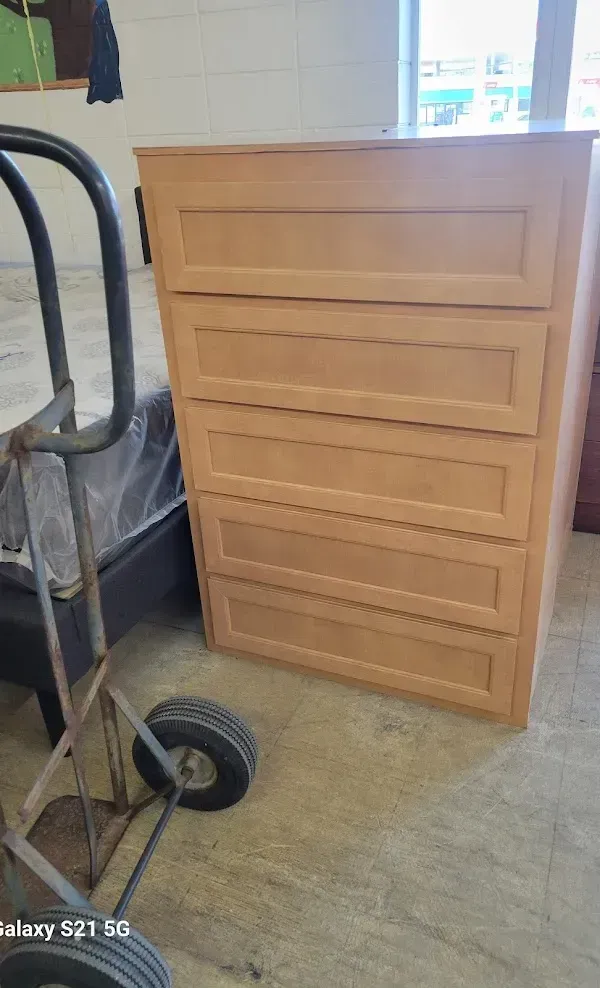 Light wood dresser with four drawers in a room, beside a hand truck near a window.
