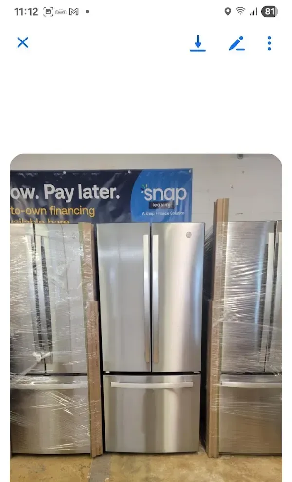 Silver four-door refrigerator displayed in an appliance store aisle, flanked by other wrapped refrigerators.