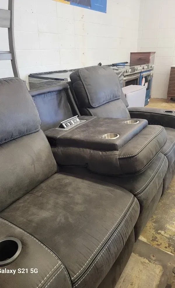 Dark gray reclining sofa with cup holders in a room against a white cinder block wall.