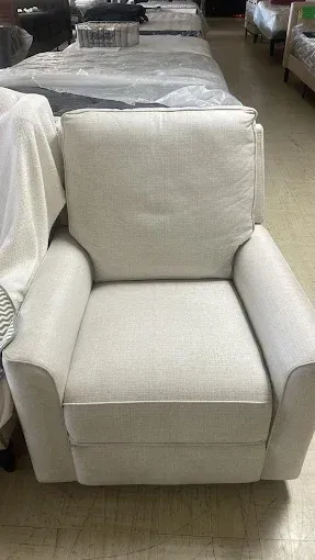 White upholstered armchair with wide arms and square cushion, shown in a furniture store aisle