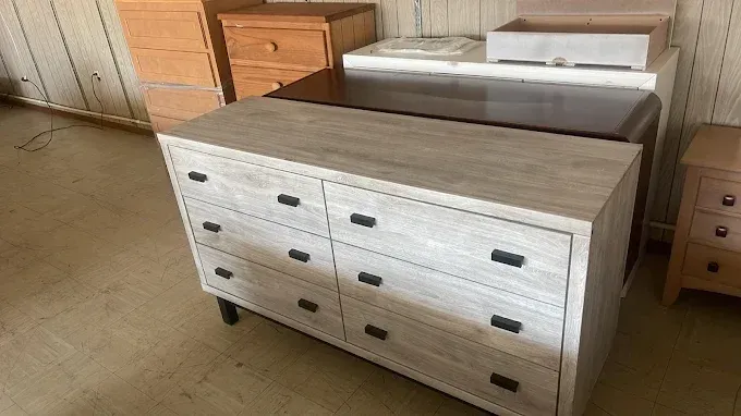 Light wood dresser with six drawers and black handles in a furniture showroom