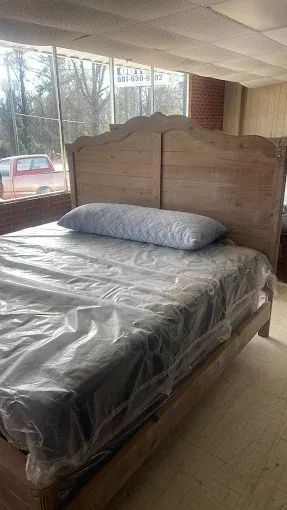 Bed with gray bedding and a wooden headboard in a room with large windows and trees outside