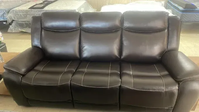 Brown leather loveseat with three back cushions and visible stitching in a showroom.