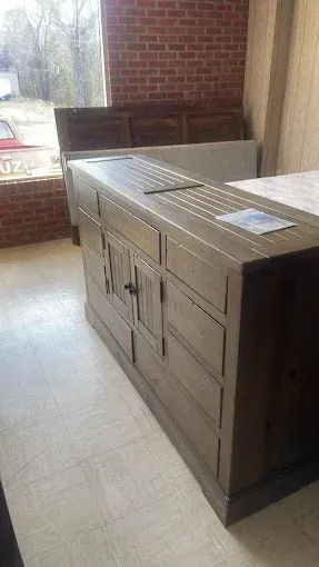 Wooden sideboard cabinet on a tiled porch beside a brick wall and screen door.