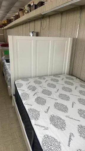 White headboard beside a bed with a patterned mattress in a small bedroom or showroom.