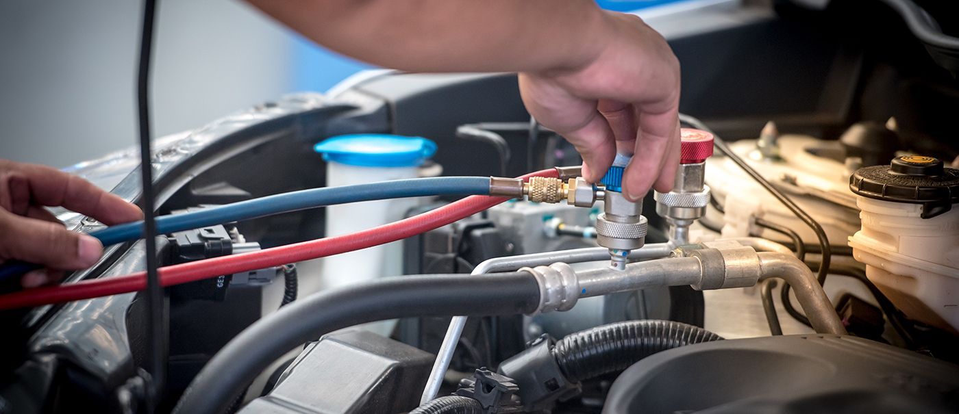A mechanic's hands connecting hoses to a car's AC system in an engine compartment.