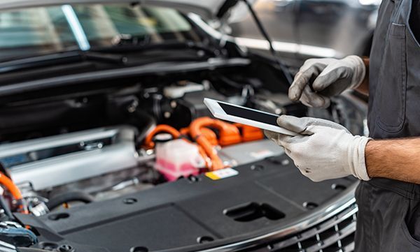 A mechanic is looking at a tablet while working on a car.