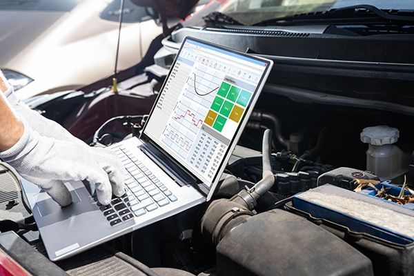 A person is using a laptop computer under the hood of a car.