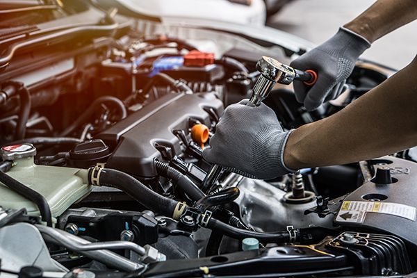 A man is working on the engine of a car with a wrench.
