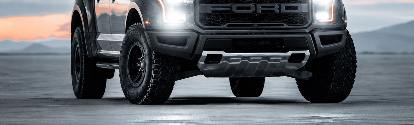 Black Ford pickup truck driving on a wet road with headlights on and snow in the background