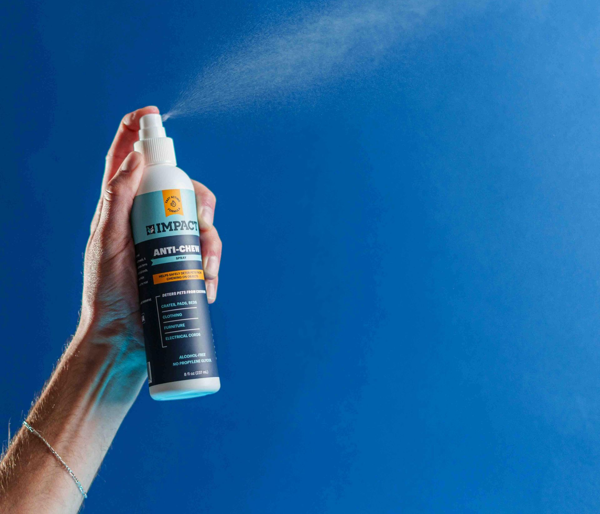 Hand holding a black-and-orange spray bottle against a blue background