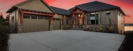 A luxury single-story house with a three-car garage and stone accents, set against a vibrant sunset sky.