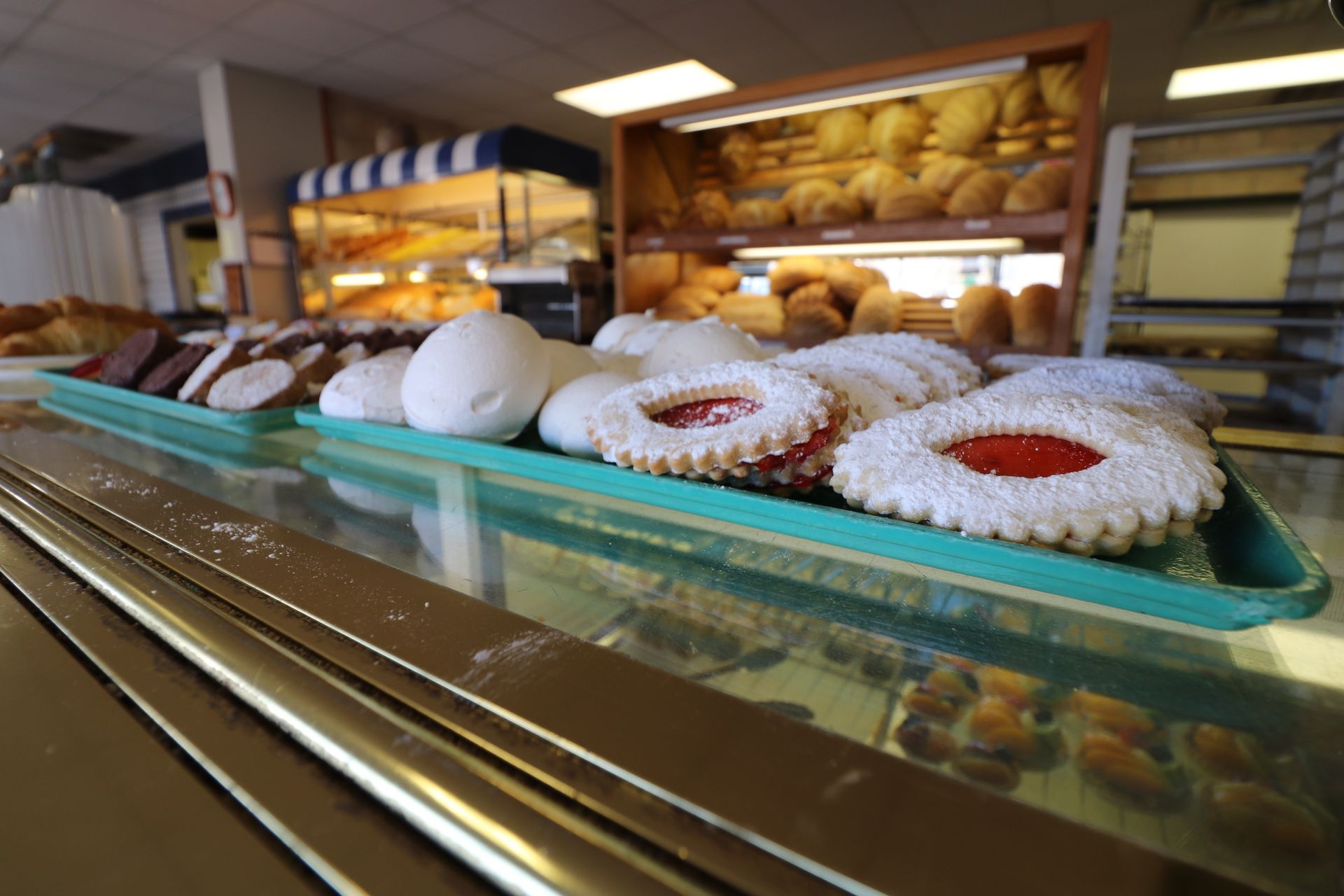 A display case in a bakery filled with trays of powdered cookies with jam centers and assorted baked goods.