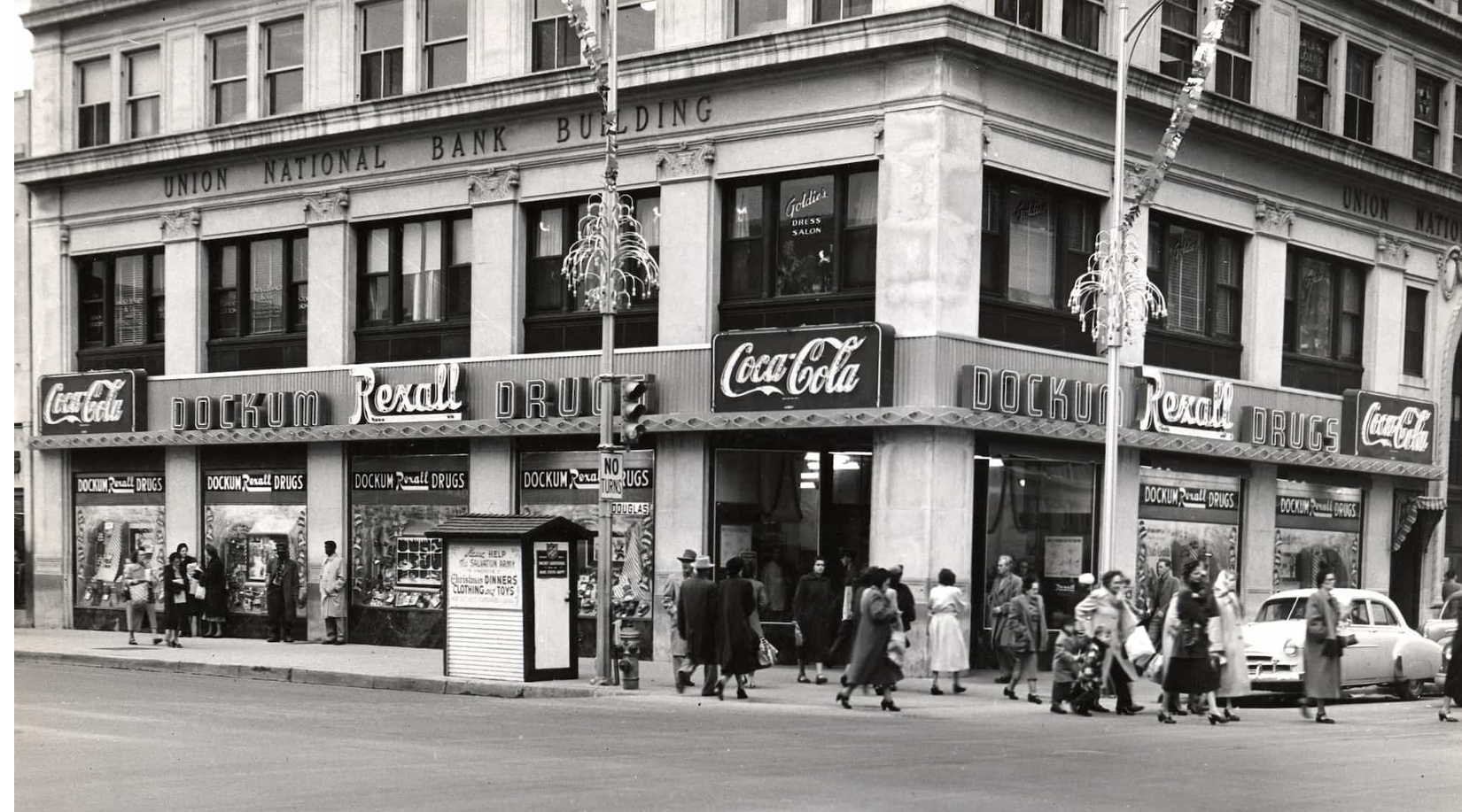 People walk along a street corner in front of the historic Dockum Rexall building 
