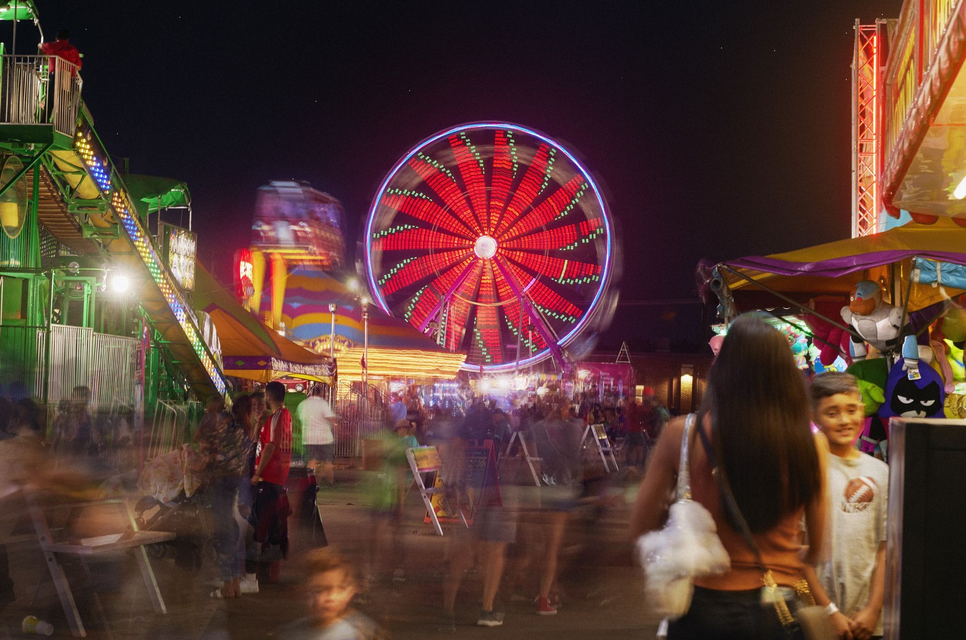 A brightly lit night at the Kansas State Fair, featuring colorful carnival rides, and a crowd of people.