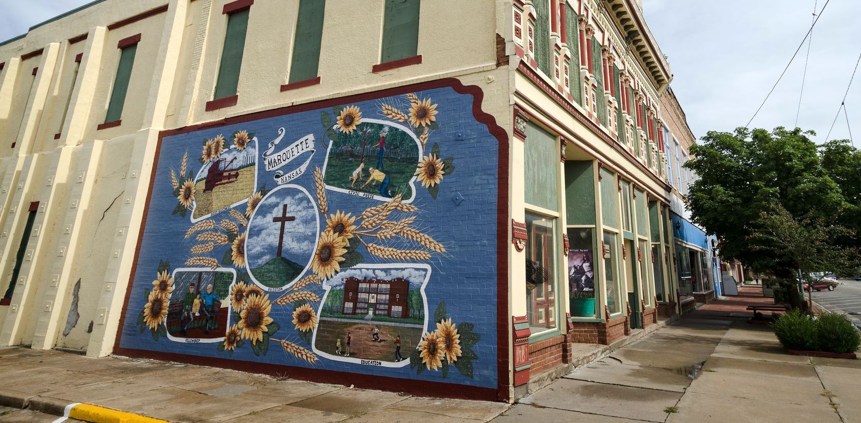 A large, colorful mural on the side of a building featuring a cross, sunflowers, and smaller painted scenes.