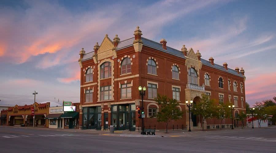 Historic red brick opera house building with arched windows stands under a colorful sunset sky in McPherson, Kansas