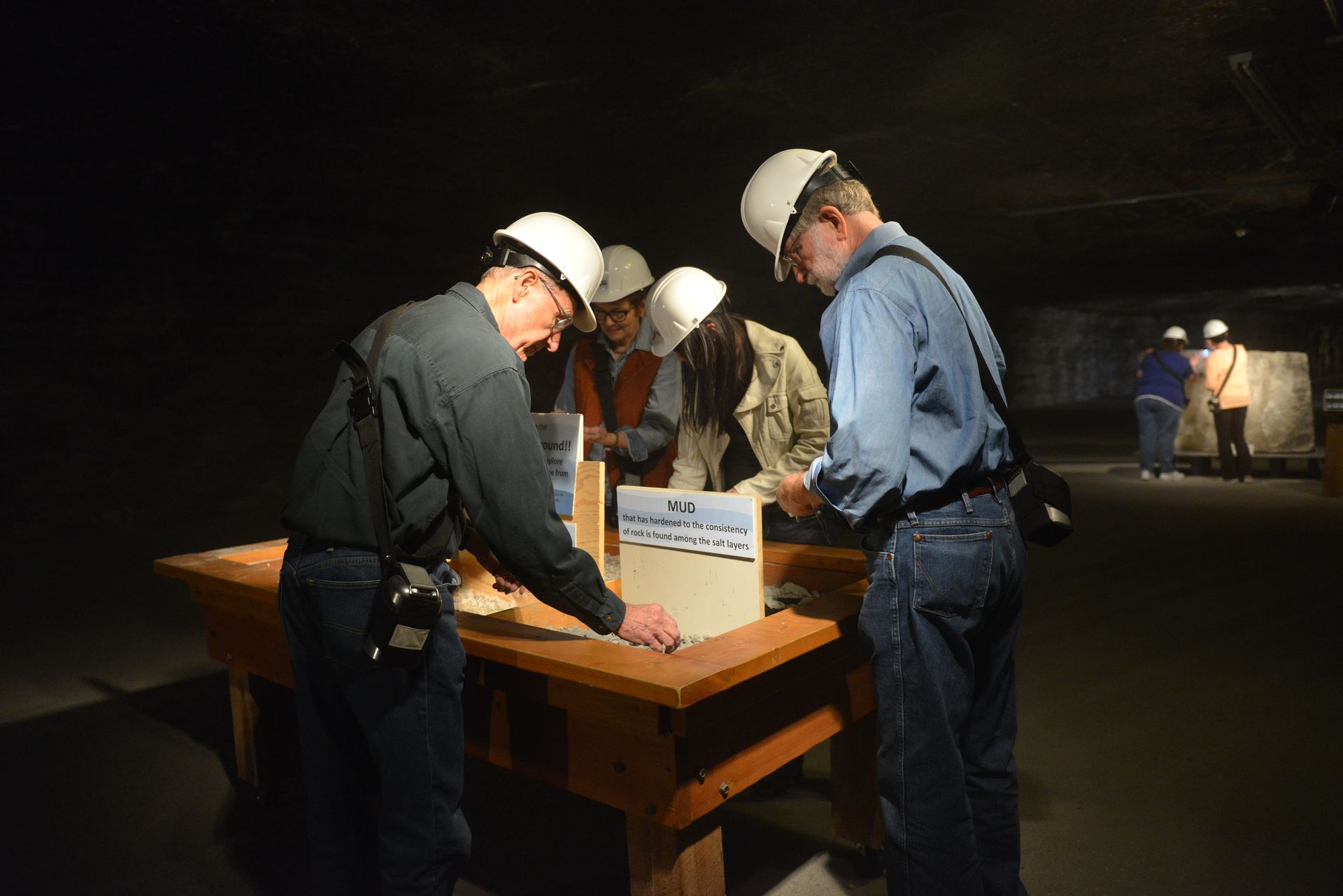 People in hard hats gather around a wooden table, examining items on display at Strataca in Hutchinson, Kansas.