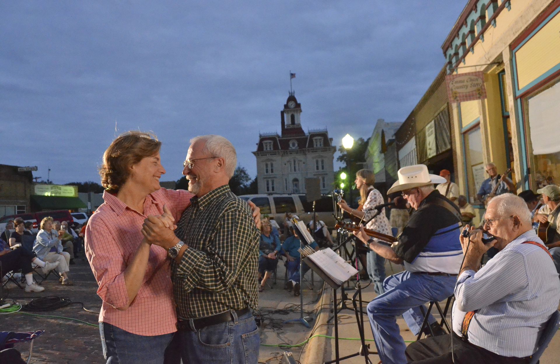 A couple dances outdoors in a town square at dusk while a small musical group performs nearby.