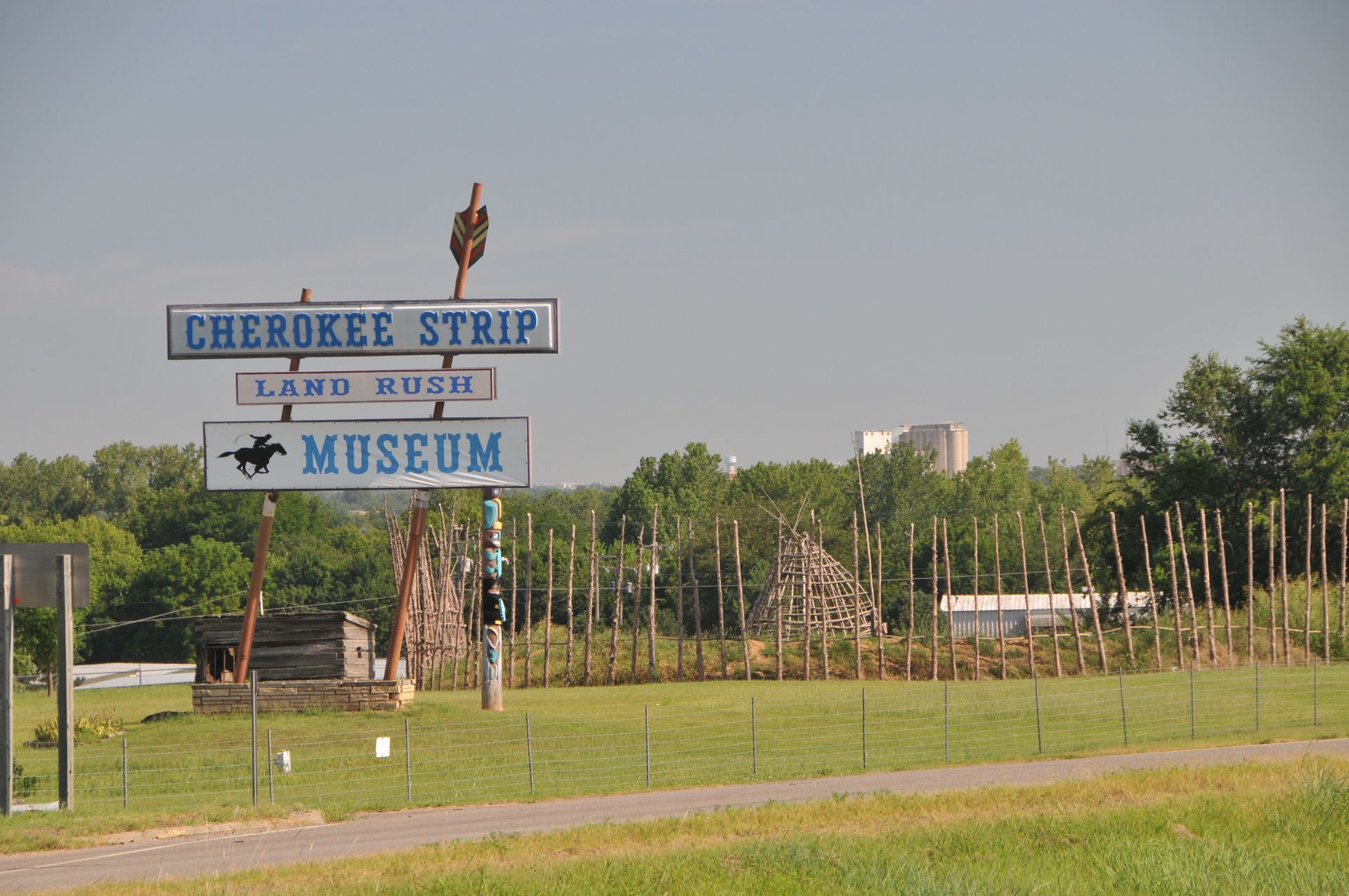 A roadside sign for the Cherokee Strip Land Rush Museum, featuring blue text on white boards, set in a grassy field.
