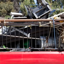Red pickup truck carrying a large metal rack and piled scrap in the bed outdoors