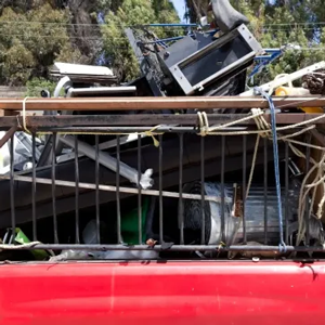 Red pickup truck carrying a large metal rack and piled scrap in the bed outdoors