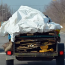 Truck hauling an overloaded pile of scrap and a white tarp on a road